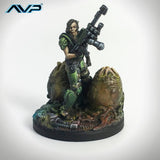 Statue of a character in green armor with a weapon, standing on a rock, on a white background with 'AVP' logo.